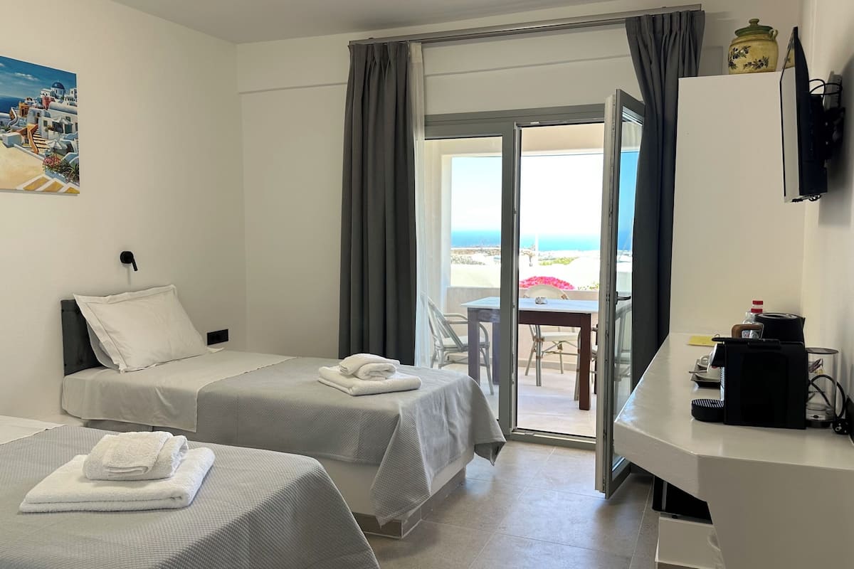 A hotel room with two beds, a desk, a TV, and a view of the sea.