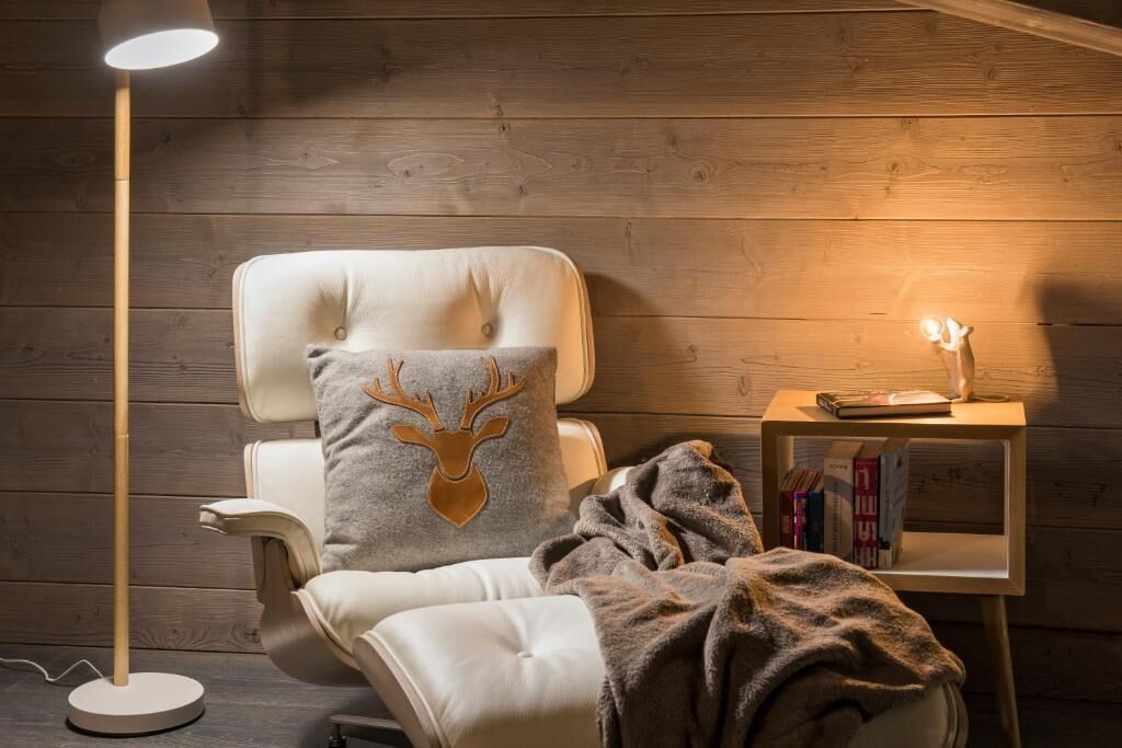Une pièce chaleureuse avec un fauteuil en cuir, une couverture, une petite table avec des livres et une lampe sur pied.