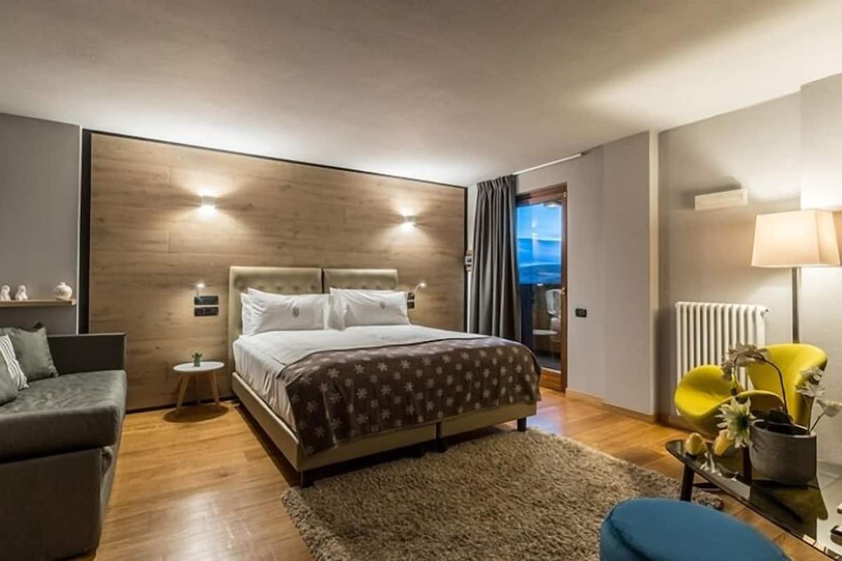 A modern bedroom with a large bed, a sofa, a small table, and a lamp.