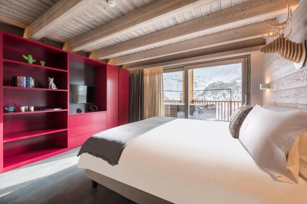 A bedroom with a bed, a red shelving unit, and a view of a snowy mountain.