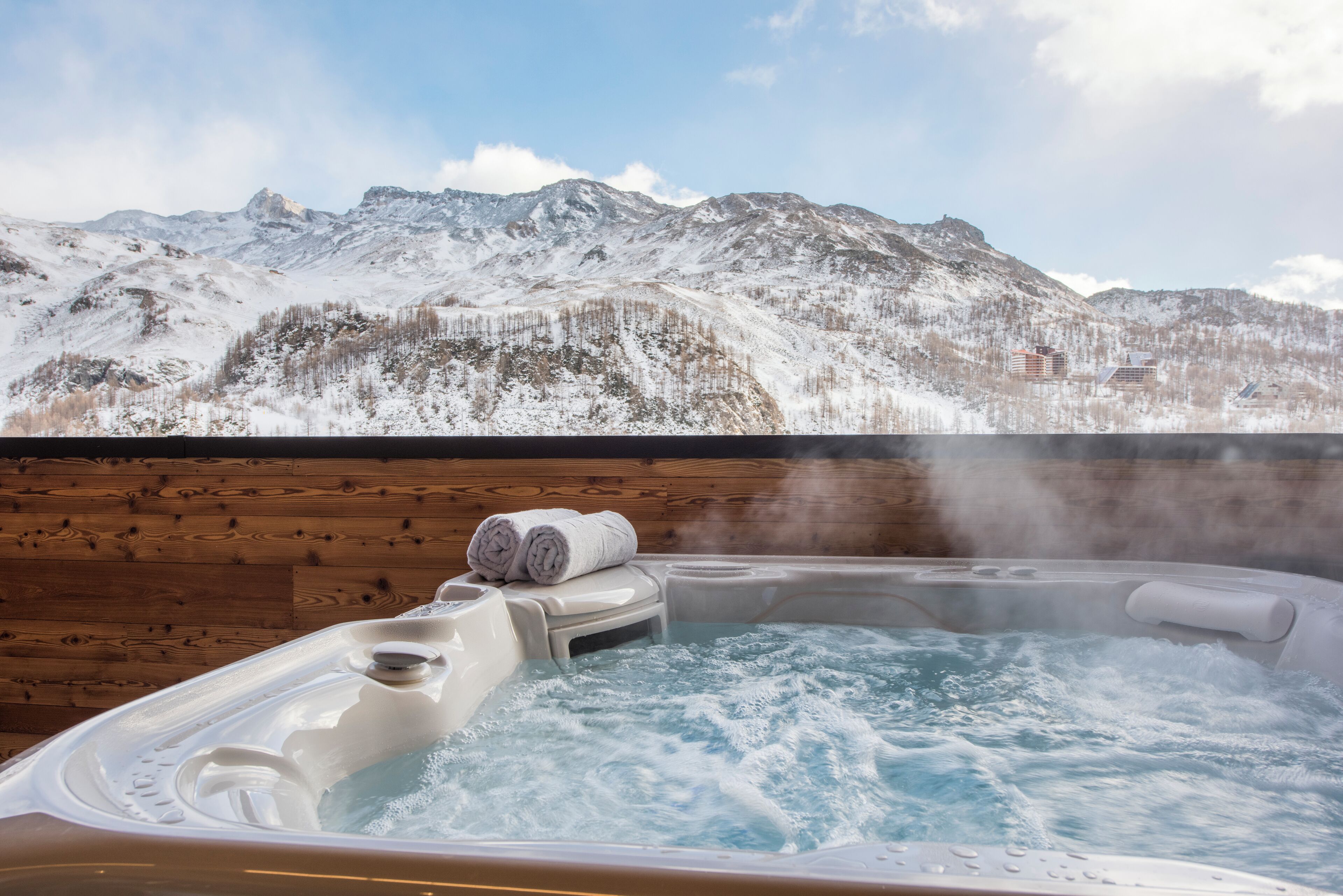 Un bain à remous avec un intérieur en bois et une vue sur des montagnes enneigées.