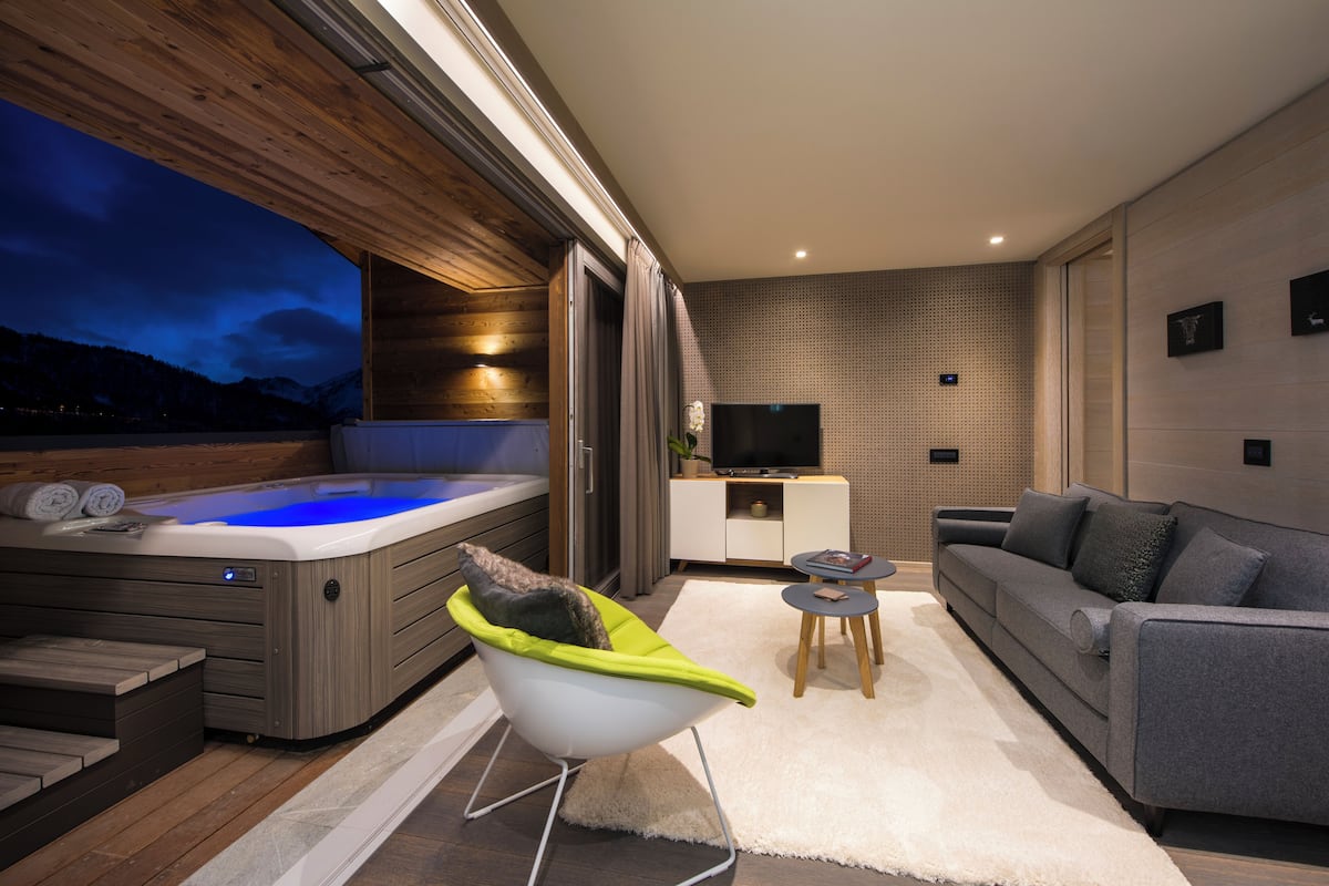 A modern living room with a hot tub, a grey sofa, a white armchair, and a flat-screen TV on a white cabinet.
