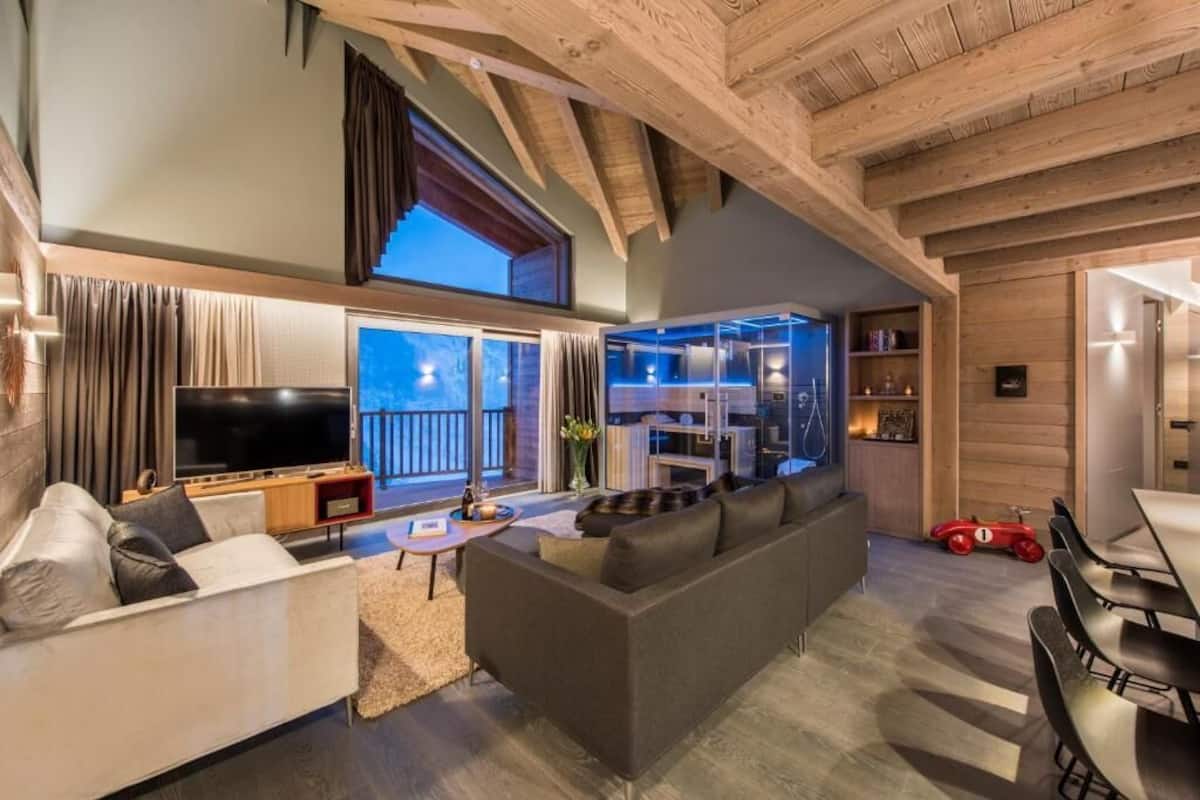 A modern living room with a large TV, a sofa, and a dining area with chairs.