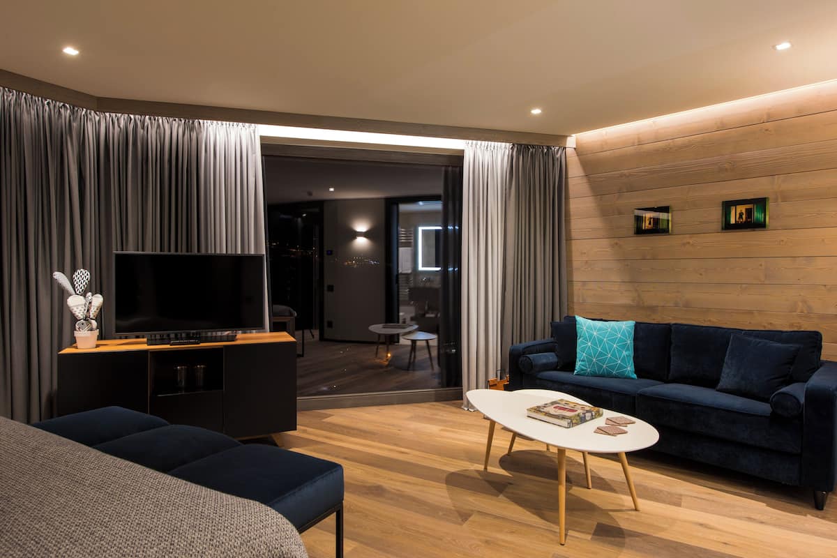A modern living room with a flat-screen TV, dark blue sofa, and a white coffee table.