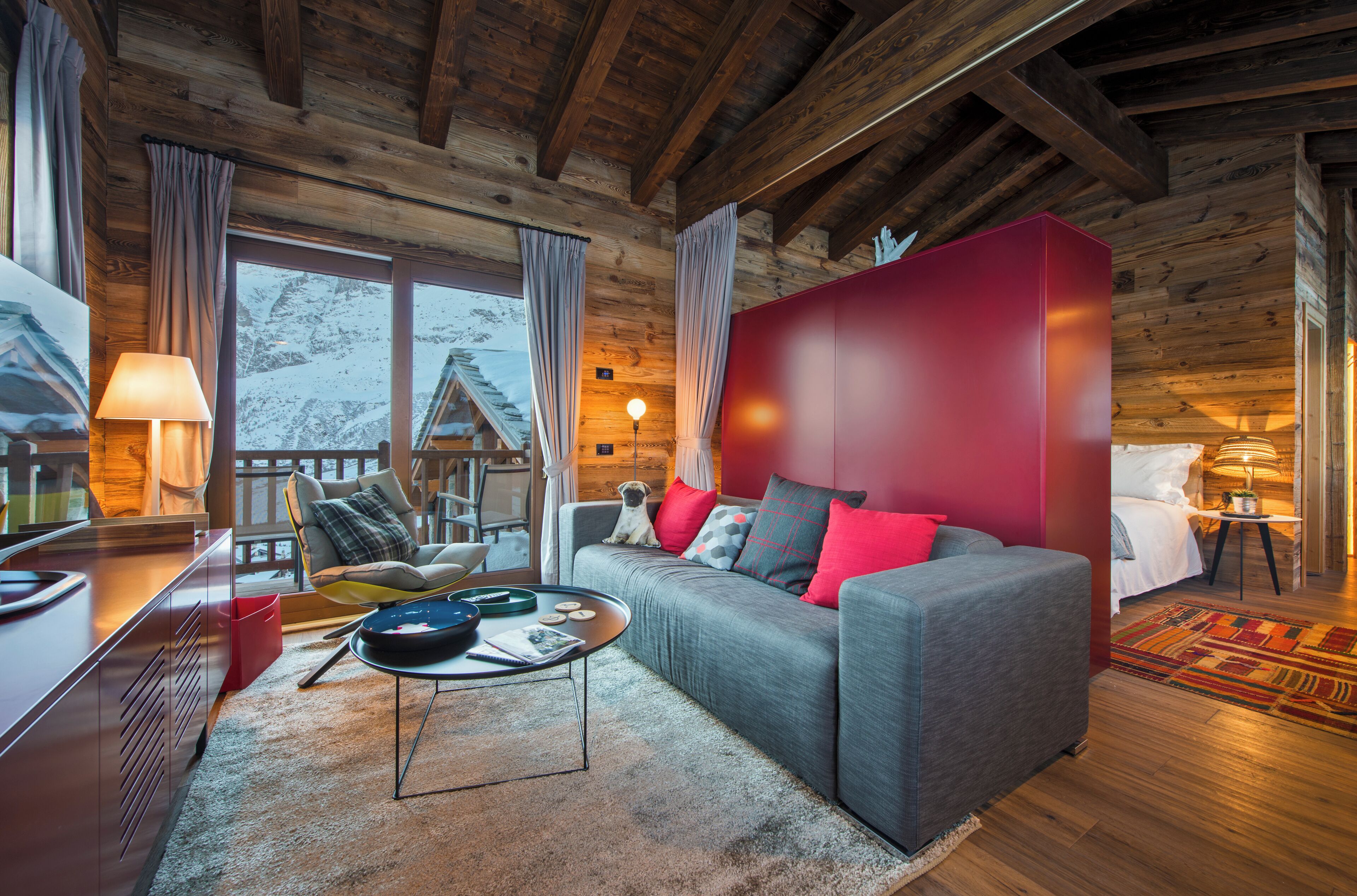 Een knus blokhutinterieur met een bank, een bijzettafeltje en uitzicht op het besneeuwde landschap.