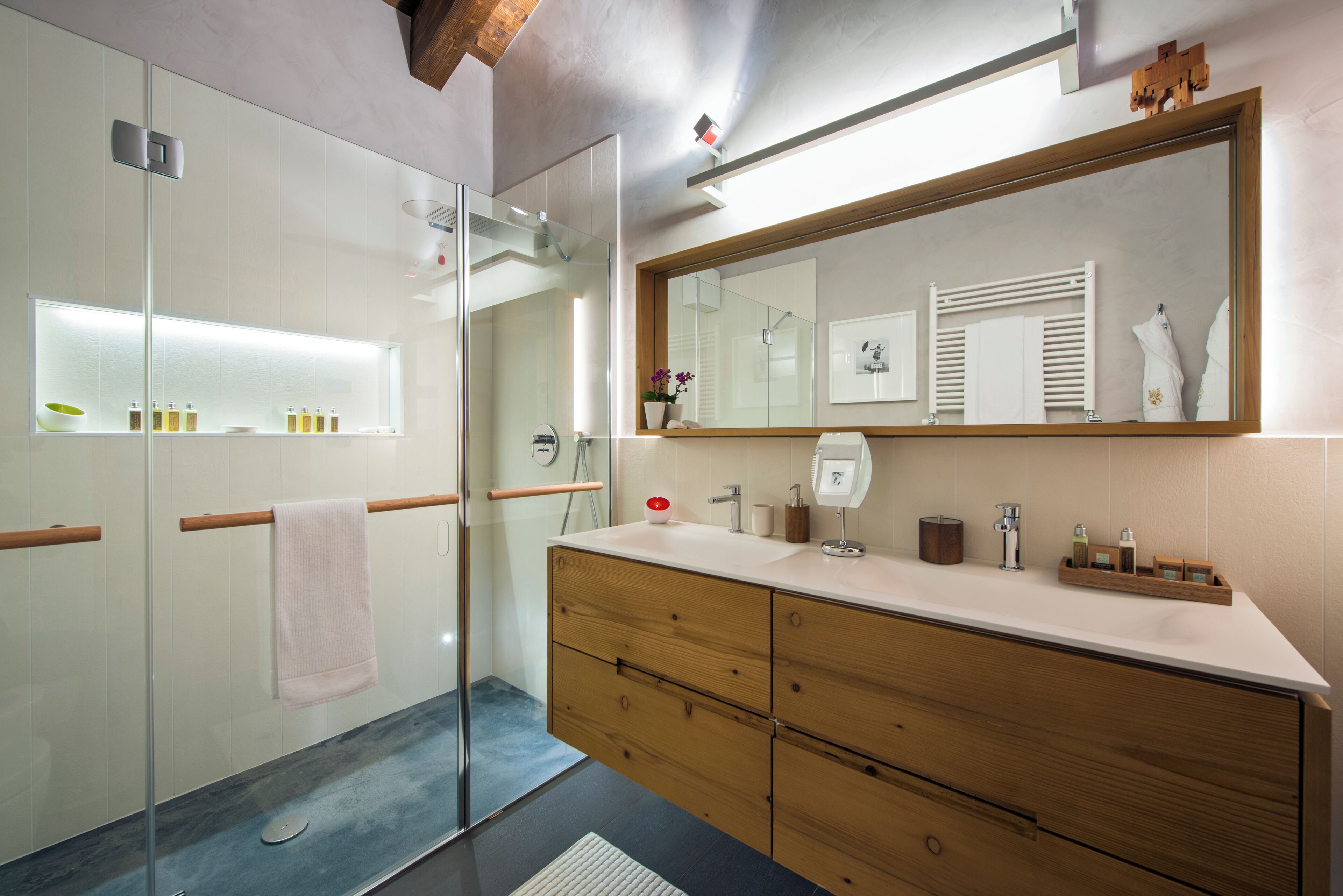 Un baño moderno con cabina de ducha de vidrio, tocador de madera y un espejo grande.