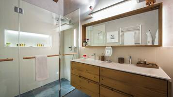 Un baño moderno con cabina de ducha de vidrio, tocador de madera y un espejo grande.
