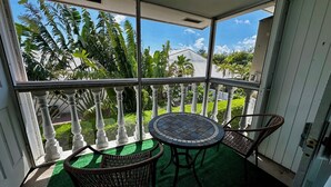 Ein überdachter Balkon mit einem runden Tisch und zwei Korbstühlen, mit Blick auf einen üppigen Garten und eine Wohngegend.