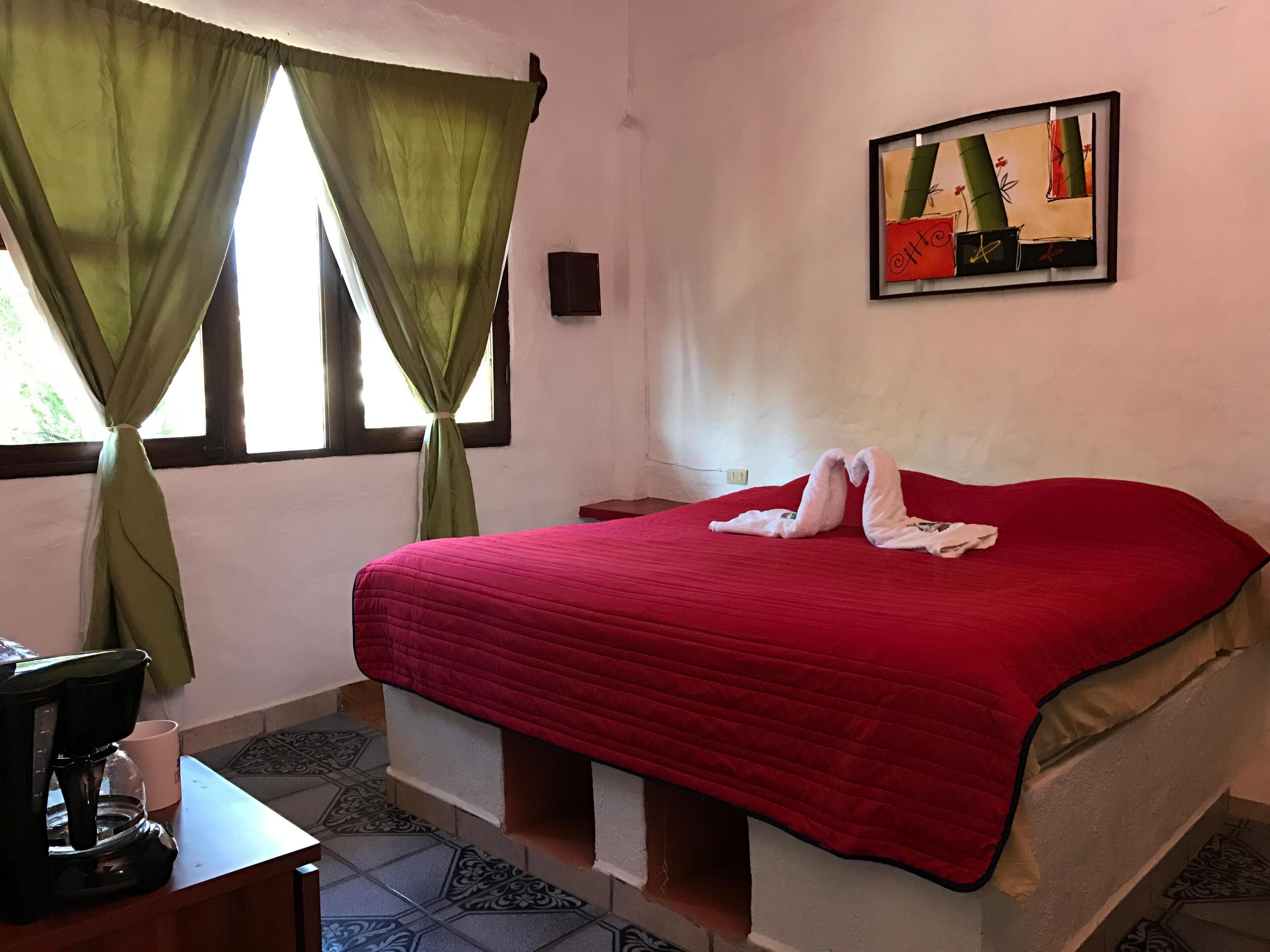 Una habitación de hotel con una colcha roja, una cafetera en una mesa y un cuadro en la pared.