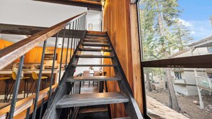 A wooden staircase leading to a dining area with a view of trees and a building outside. - Kingswood Village Escape – For 4 (Kings Beach)