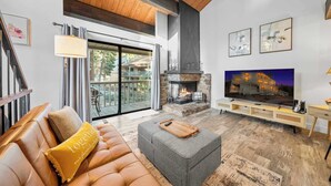 A modern living room with a fireplace, a sofa, a coffee table, and a TV. - Kingswood Village Escape – For 4 (Kings Beach)