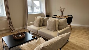 Un salon moderne avec un canapé beige, une table basse noire et un coin repas comprenant une table et des chaises.