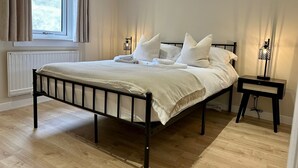 Un lit bien fait, avec du linge de lit blanc et des oreillers, une table de chevet avec une lampe et une fenêtre avec des rideaux.