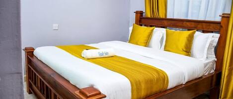 Una cama individual con estructura de madera, ropa de cama blanca y amarilla, y una almohada con una toalla.