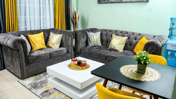 A living room with two grey sofas, yellow cushions, a white coffee table, and a black table with a plant. - Vimally Suites Naivasha (Naivasha)