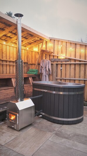 A wood-floored outdoor area with a wood-burning stove, a hot tub, and a hanging robe. - The Stone Barn (Login)