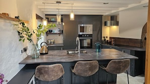 A modern kitchen with a central island, bar stools, a kettle, and a toaster. - The Stone Barn (Login)