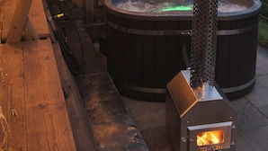 An outdoor hot tub area with a wood-burning stove and a wooden deck. - The Stone Barn (Login)