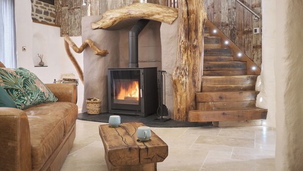 A cozy living room with a fireplace, a wooden staircase, and a leather sofa. - The Stone Barn (Login)