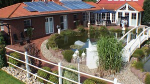 Una casa con techo solar, un estanque y un puente.