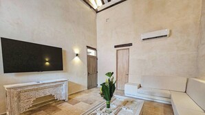 Un salon doté d’un téléviseur à écran plat, d’un canapé blanc, d’une table basse à motifs et d’un vase décoratif contenant des fleurs.