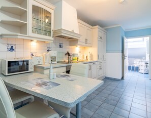 Een moderne keuken met witte kasten, een granieten aanrechtblad en een eethoek met een witte stoel.