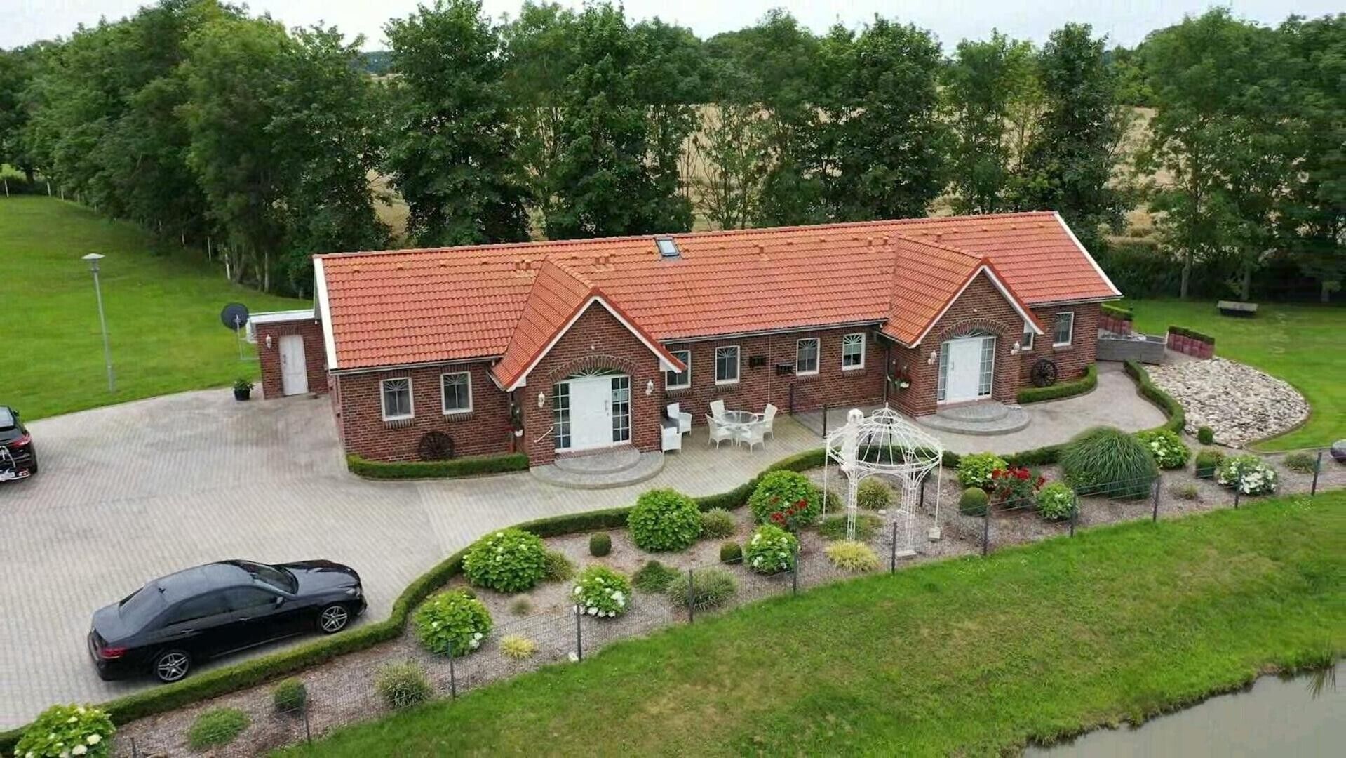 Een herenhuis met twee verdiepingen, een met rode tegels bedekte dak, een oprit en een aangelegde tuin met een pergola.
