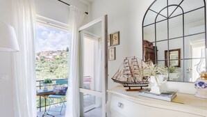 Ein Zimmer mit großem Fenster, einem Schminktisch mit Schubladen, einem Spiegel und einem Schiffsmodell.