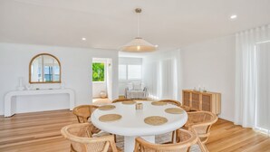 Une salle à manger moderne avec une table ronde, des chaises en osier et un buffet blanc agrémenté d’un miroir.