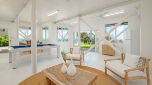 Une pièce spacieuse et bien éclairée, équipée d’une table de billard, de sièges confortables et de grandes fenêtres offrant une vue sur l’extérieur.