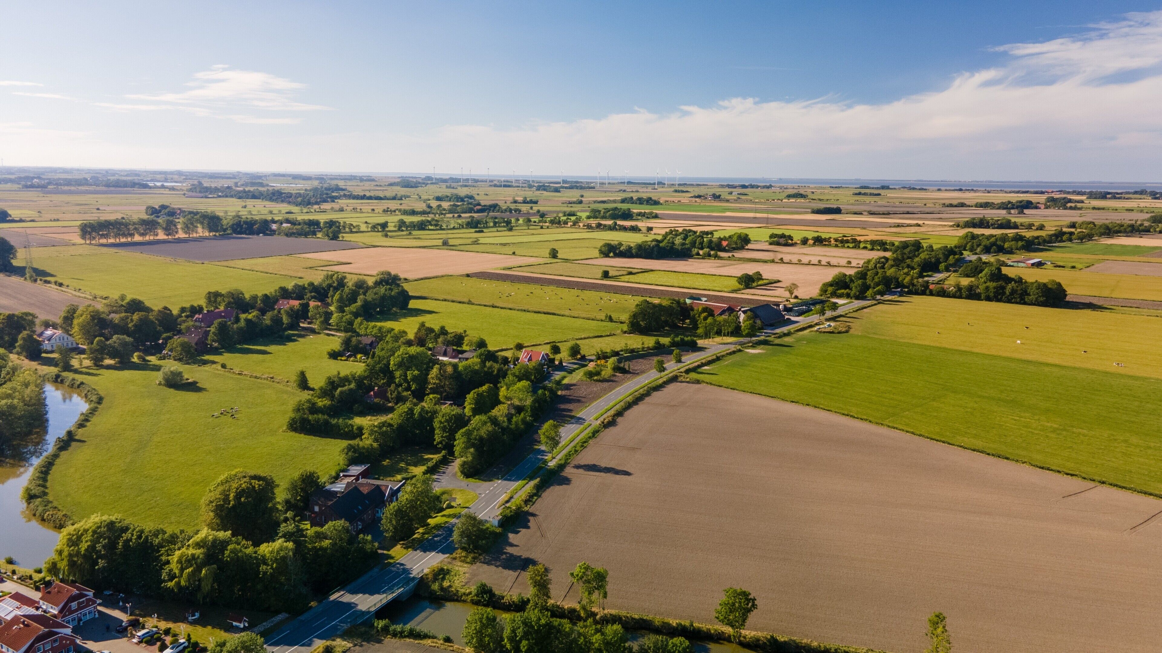 An aerial view of a rural landscape with fields, a river, and a bridge.