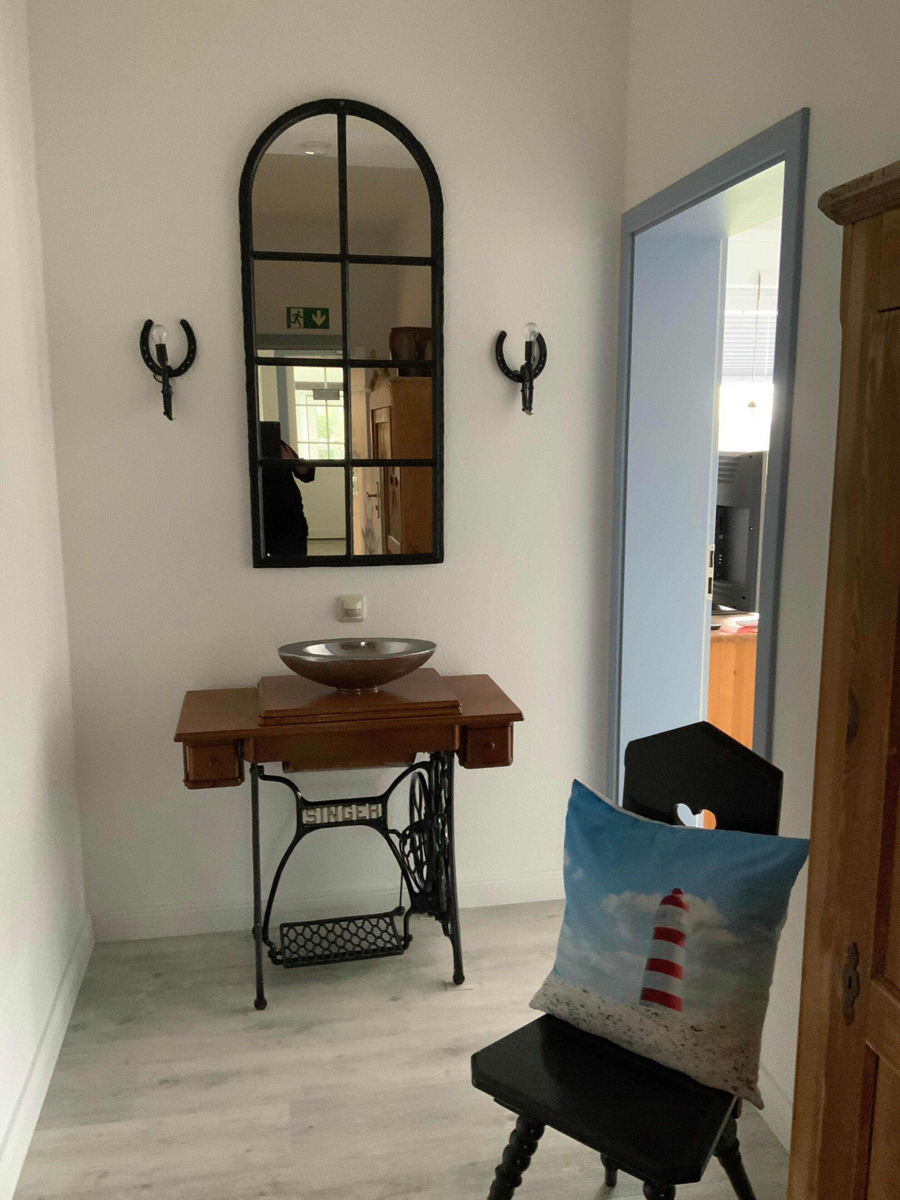 Une pièce comprenant une table en bois, une machine à coudre, un miroir et une chaise avec un coussin.