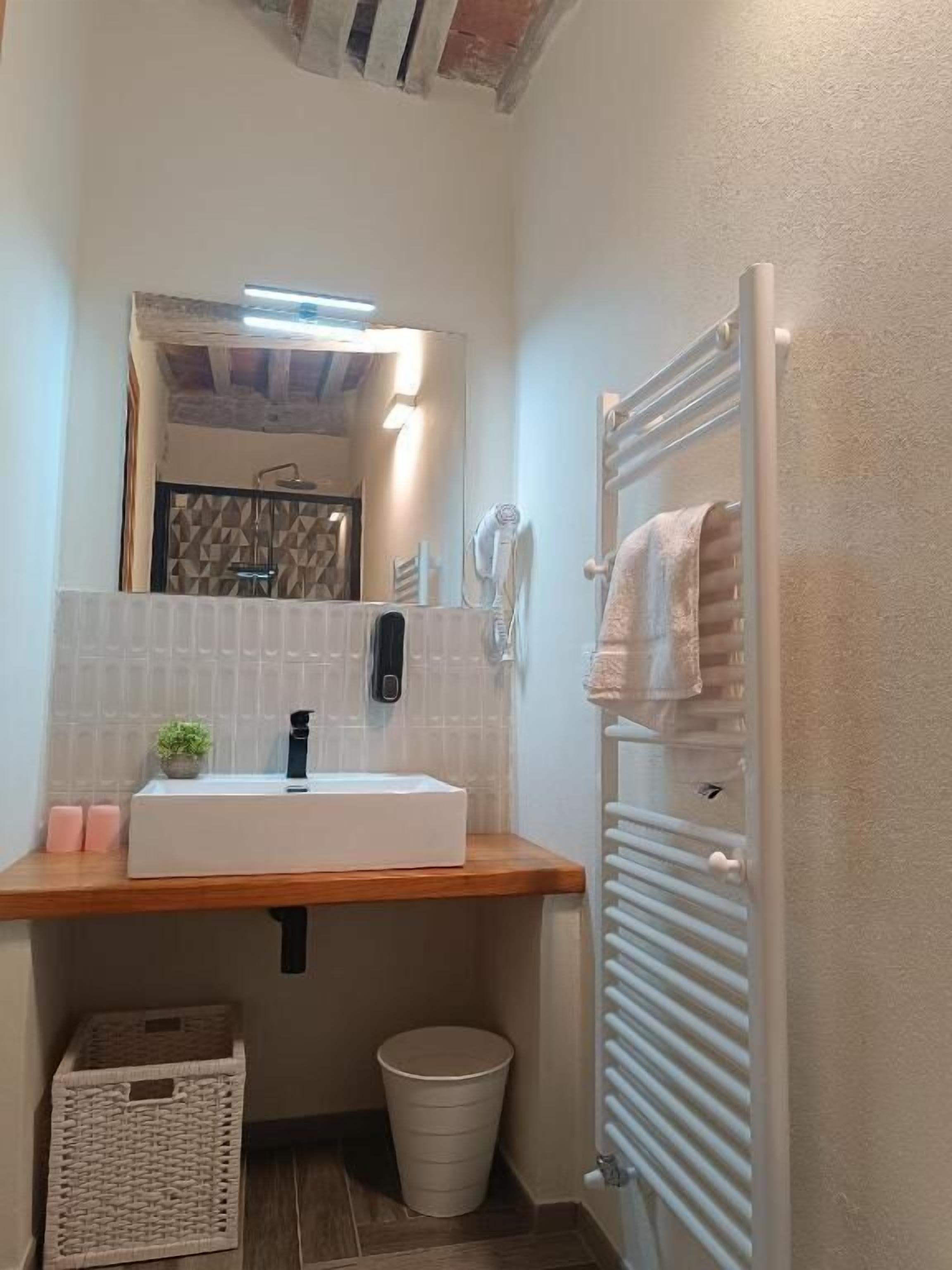 Une petite salle de bain avec un lavabo blanc, un miroir, un porte-serviettes et une petite poubelle.