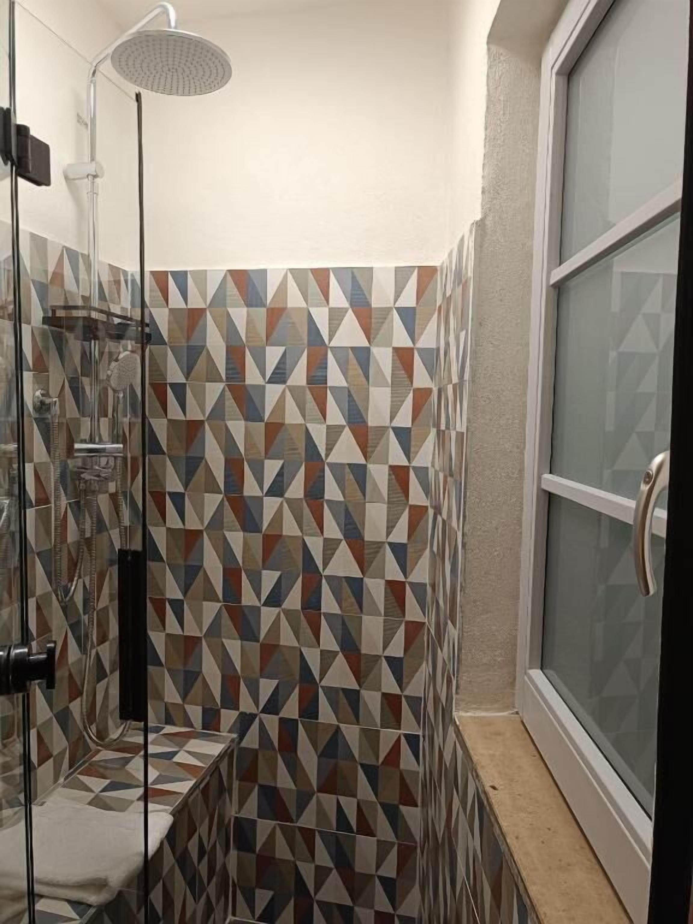 A shower with a rain showerhead, a glass enclosure, and a geometric-patterned wall.