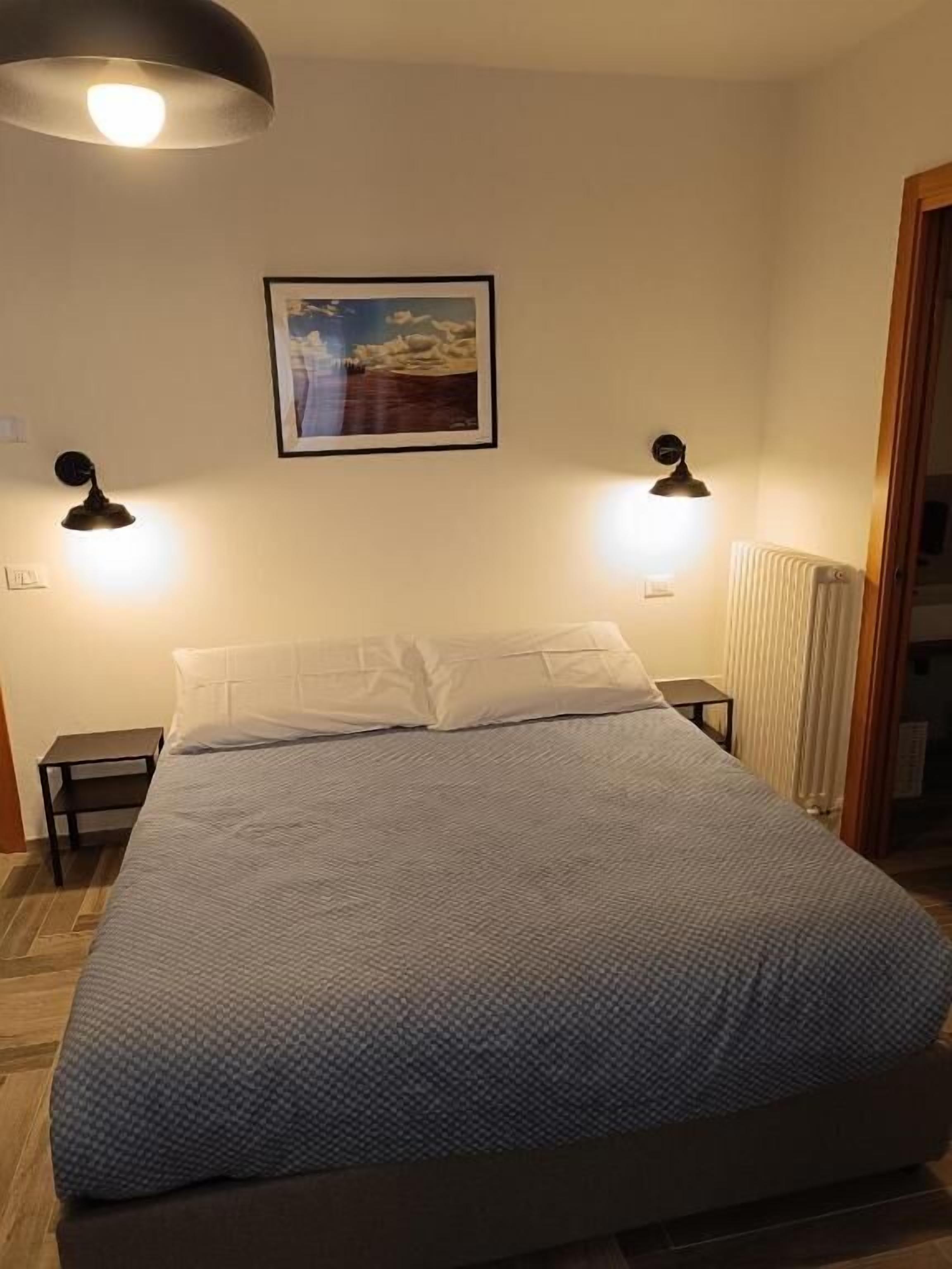 Een slaapkamer met een bed, twee bedlampen, een lijst met een afbeelding aan de muur, en een radiator.