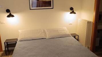 Een slaapkamer met een bed, twee bedlampen, een lijst met een afbeelding aan de muur, en een radiator.