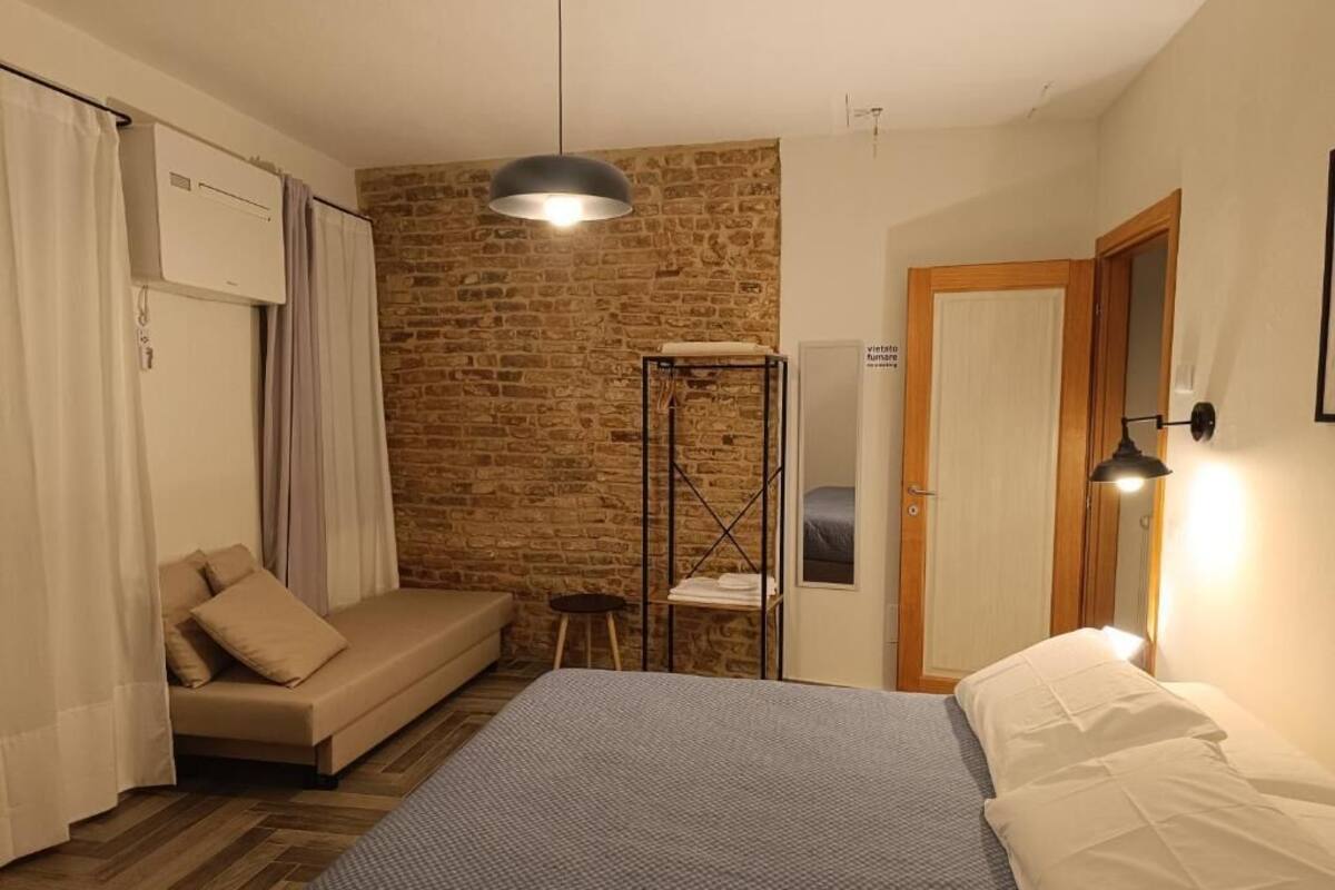 Un dormitorio con una cama, un sofá, un taburete pequeño, un armario y una pared de ladrillo.