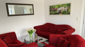 A room with a red sofa set, a glass coffee table, a vase with flowers, a framed picture on the wall, and a mirror. - Apartment 'Ferienwohnung 7 - Reihernest' with Shared Terrace, Wi-Fi and Air Conditioning (Wangerland)