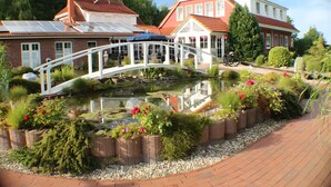 A garden with a pond, a white bridge, and a red-roofed building. - Apartment 'Ferienwohnung 7 - Reihernest' with Shared Terrace, Wi-Fi and Air Conditioning (Wangerland)