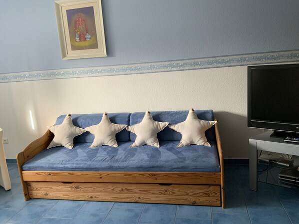 Una habitación con sofá azul, almohadas con forma de estrella, un cuadro en la pared y un televisor sobre un mueble.