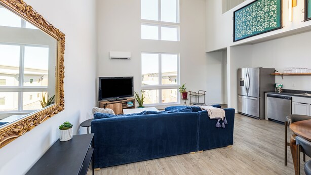 Eine moderne Wohnung mit einem großen blauen Sofa, einem Flachbildfernseher, einer Küche mit Edelstahlgeräten und einem großen, verzierten Spiegel.