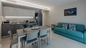 Una cocina moderna con armarios grises, una mesa de comedor con sillas, un sofá azul turquesa y un cuadro en la pared.