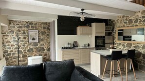Uma cozinha moderna com paredes de pedra, uma área de jantar com cadeiras pretas e um sofá preto em primeiro plano.