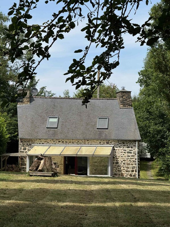 A stone house with a sloped roof, a covered porch, and a chimney.