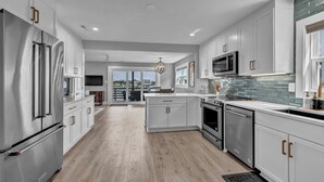 A modern kitchen with stainless steel appliances, white cabinetry, and a view to the outdoors. - The Wright View–Waterfront Escape w/ Dock | Views |Close to Dining and Shopping (Wrightsville Beach NC)