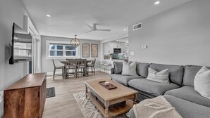 A modern living room with a grey sofa, wooden coffee table, and dining area with a wooden table and chairs. - The Wright View–Waterfront Escape w/ Dock | Views |Close to Dining and Shopping (Wrightsville Beach NC)