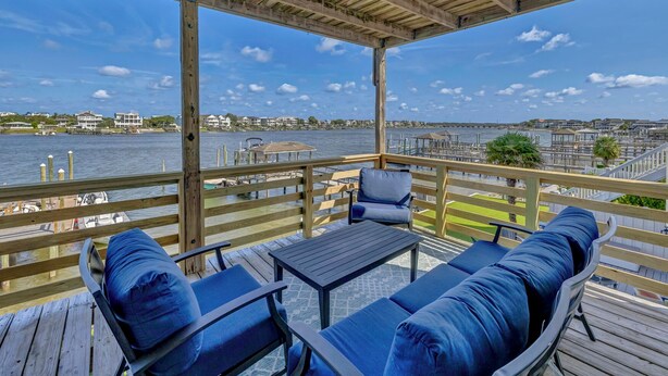 A wooden deck with outdoor seating and a view of the water and buildings in the background. - The Wright View–Waterfront Escape w/ Dock | Views |Close to Dining and Shopping (Wrightsville Beach NC)