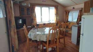 A cozy, well-lit kitchen with wooden cabinets, a dining table with chairs, and a refrigerator. - Mobil home Le Duo Tranquille (Souvigné)