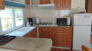A compact kitchen with wooden cabinets, a gas stove, a microwave, and a refrigerator. - Mobil home Le Duo Tranquille (Souvigné)