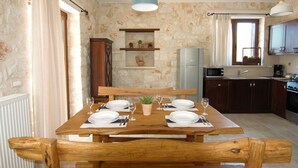 A dining area with a wooden table set for four, a small potted plant, and a stone wall backdrop. - Rosemary Cottage, Lioriza Houses Zakynthos (Zakynthos)